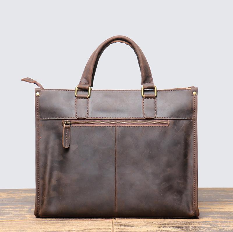 Handmade full grain leather messenger bag with top handles and exterior zipper pocket on a wooden surface