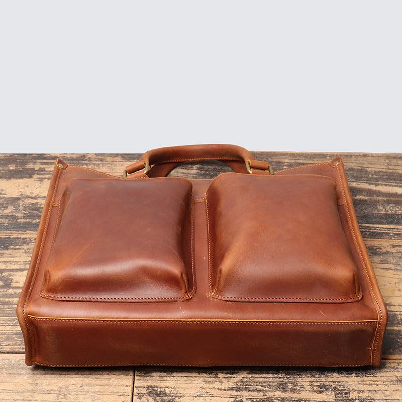 Full grain brown leather messenger bag with dual front pockets and sturdy handle on wood table
