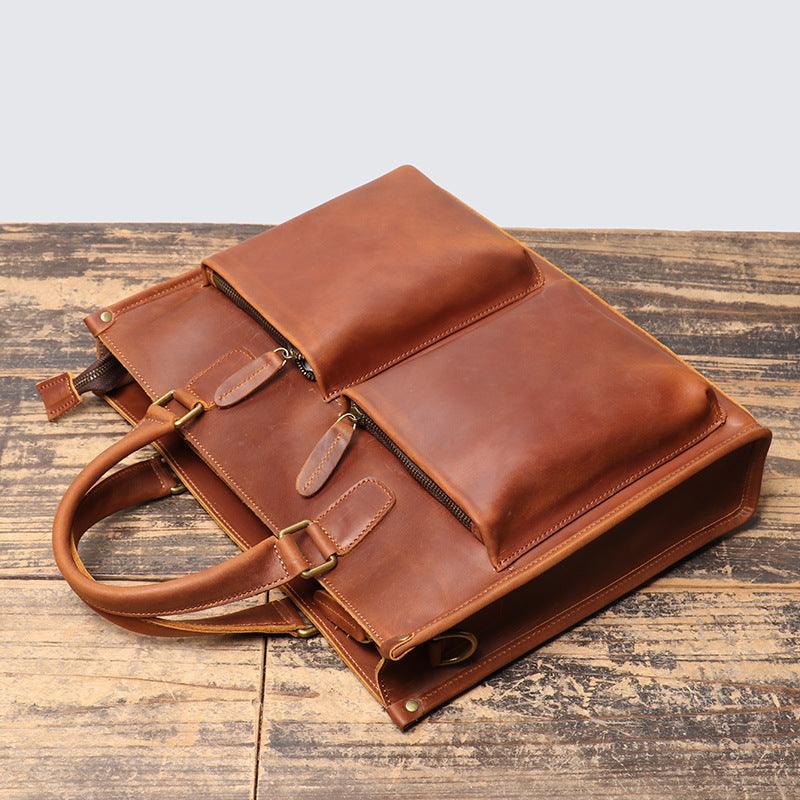 Handmade full grain leather messenger bag with top handles and front pockets on rustic wood