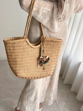 Handmade woven leather tote bag with braided handles and horse charm, worn by woman in light dress