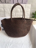 Handwoven raffia straw tote standing upright – structured natural fibre beach bag large size