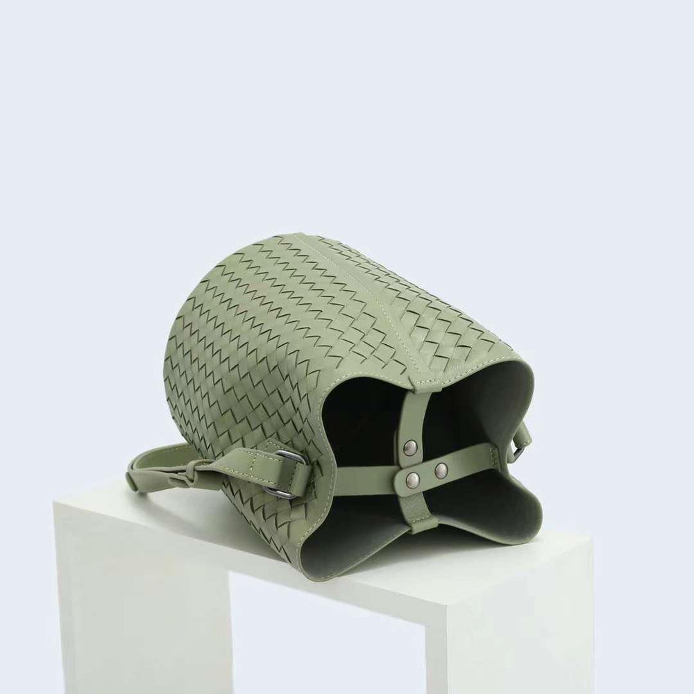 Sage green woven lambskin leather bucket bag with crossbody strap on white pedestal