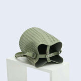 Sage green woven lambskin leather bucket bag with crossbody strap on white pedestal