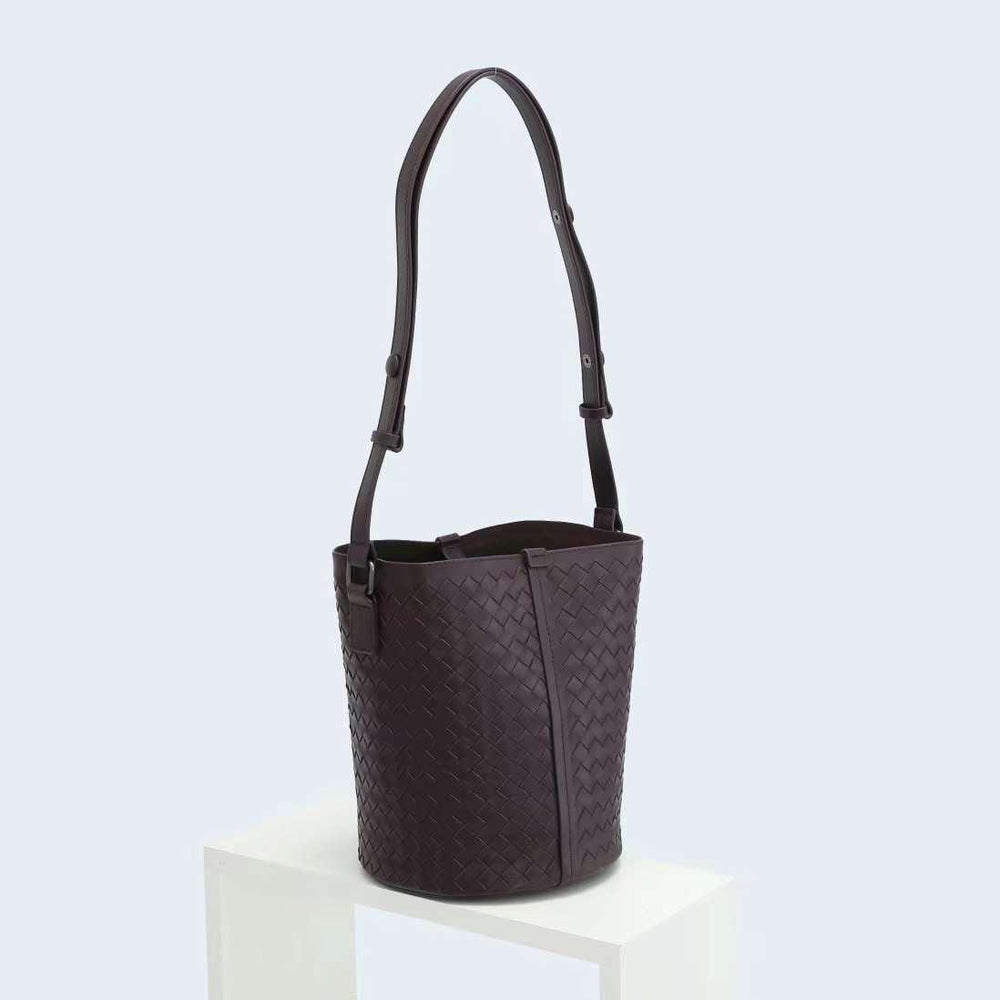 Dark brown woven lambskin leather bucket bag with adjustable shoulder strap on display stand