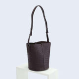 Dark brown woven lambskin leather bucket bag with adjustable shoulder strap on display stand