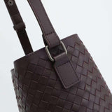 Close-up of a woven dark brown lambskin leather bucket bag with adjustable shoulder strap