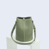 Sage green woven lambskin leather bucket bag with adjustable shoulder strap on white pedestal