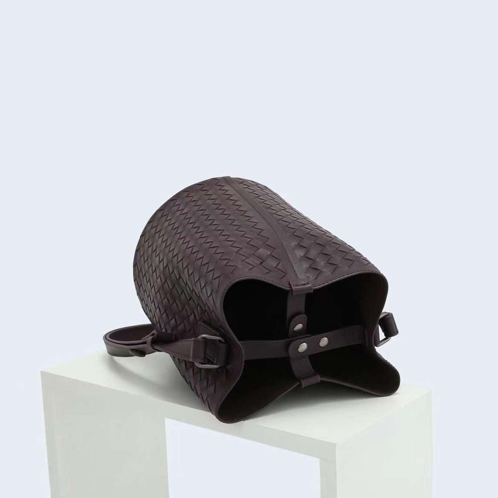 Woven lambskin leather bucket bag with adjustable strap, displayed on a white stand.