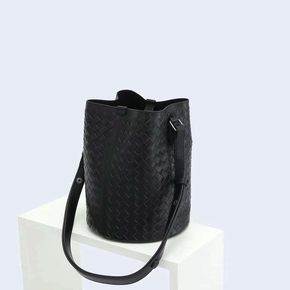 Black woven lambskin leather bucket bag with adjustable shoulder strap on white display