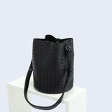 Black woven lambskin leather bucket bag with adjustable shoulder strap on white display