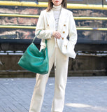 Woman in white suit carrying large green woven lambskin leather tote bag