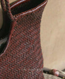 Close-up of a woven brown cowhide leather handbag with bamboo-style handle