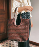 Woman holding brown woven leather tote bag with braided handles, ideal for summer and casual outings