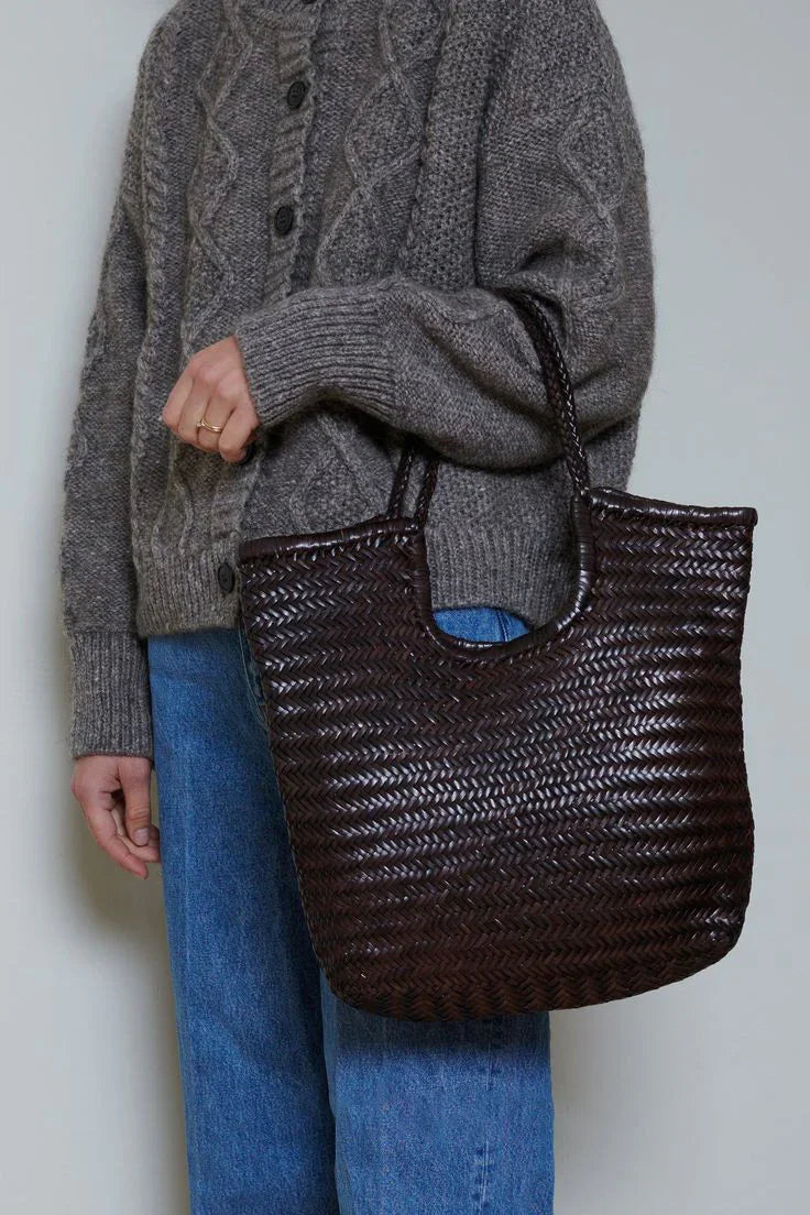 Woman holding a large dark brown woven leather tote bag with double handles.