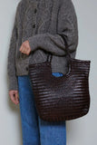 Woman holding a large dark brown woven leather tote bag with double handles.