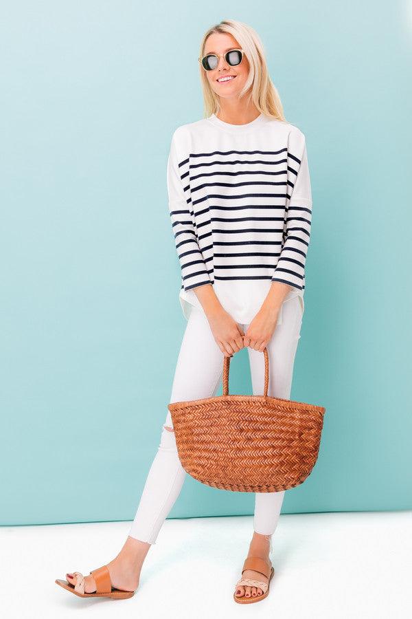 Woman holding large woven leather handbag, wearing striped top and white pants