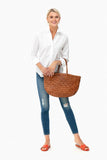Woman holding large brown woven leather basket handbag, wearing white shirt and jeans