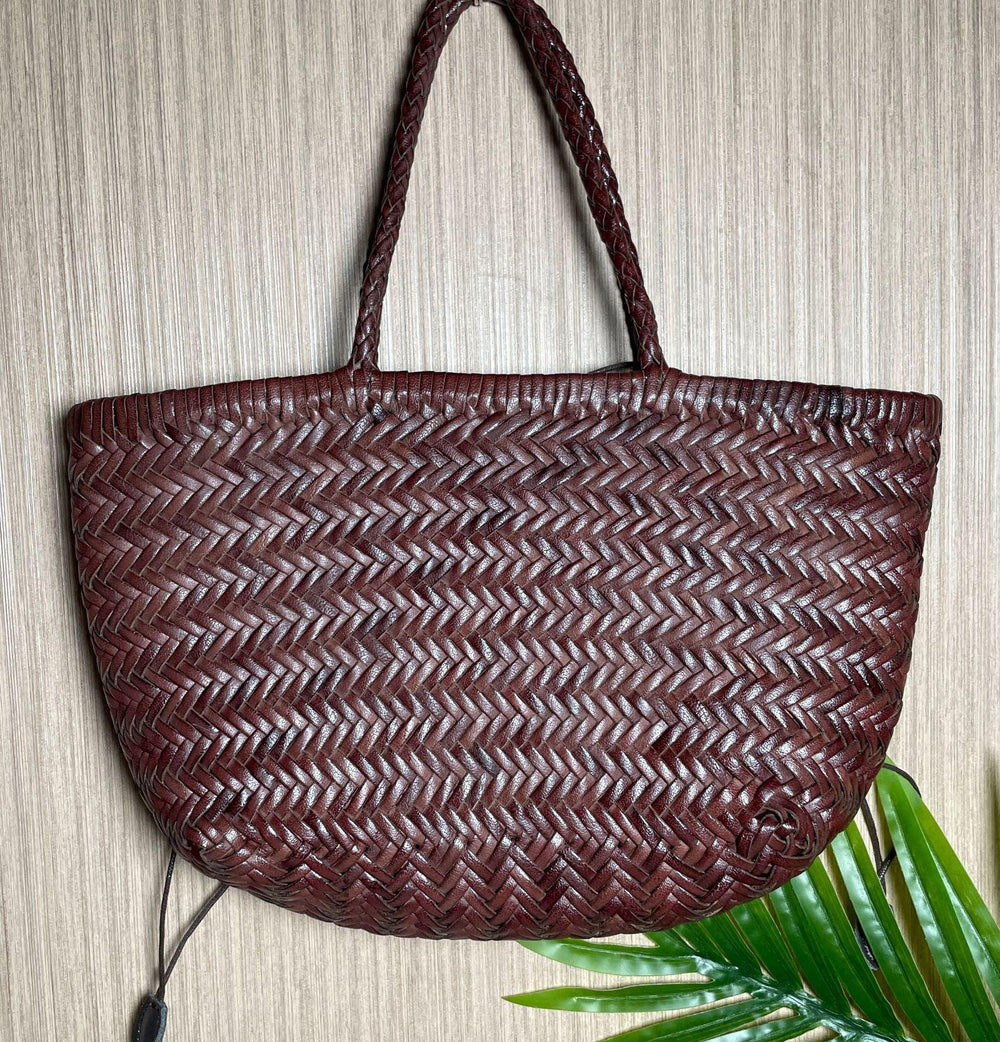 Handcrafted brown woven leather handbag with bamboo-style handles on a neutral background