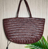 Handcrafted brown woven leather handbag with bamboo-style handles on a neutral background