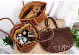 Handcrafted woven leather handbags in brown shades, with one bag open showing cosmetics inside