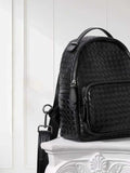 Small black lambskin leather backpack with handwoven pattern and silver zippers on white pedestal