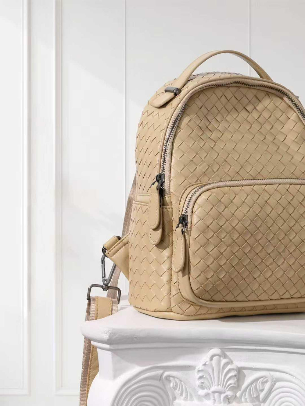 Beige woven lambskin leather small backpack with front pocket and top handle on white background