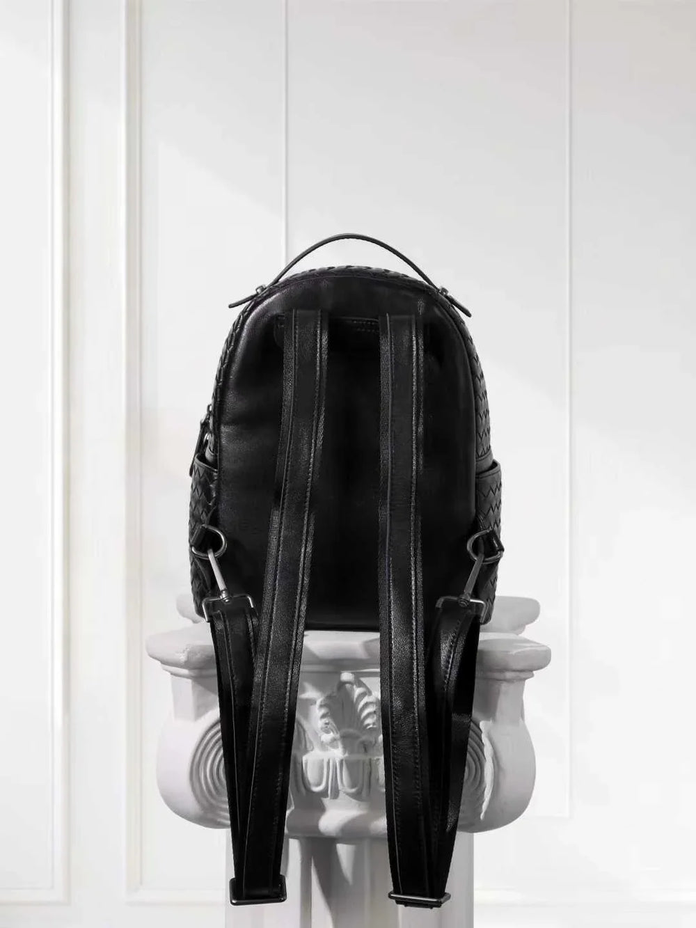 Black woven lambskin leather backpack with adjustable straps on a white pedestal
