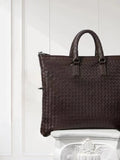 Black intrecciato woven lambskin leather tote bag with top handles, displayed on pedestal