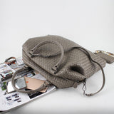 Taupe woven leather tote bag with top handles and shoulder strap, displayed on magazines.