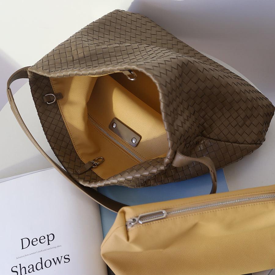 Open woven leather tote bag with yellow lining and zip pouch on a white table.
