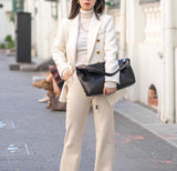 Woman wearing a white blazer holding a large black woven leather tote bag on city street