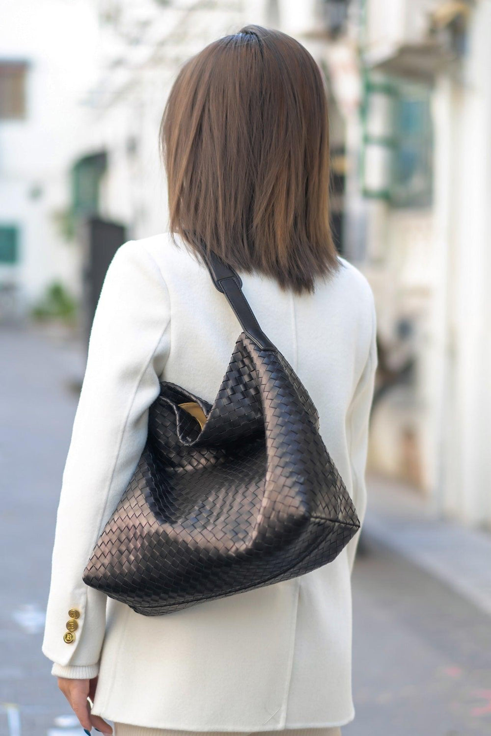 Woman wearing a white coat with a large black woven leather shoulder tote bag
