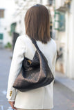 Woman wearing a white coat with a large black woven leather shoulder tote bag
