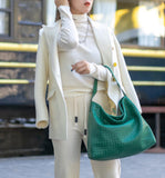 Woman in white outfit carrying large green woven leather tote shoulder bag