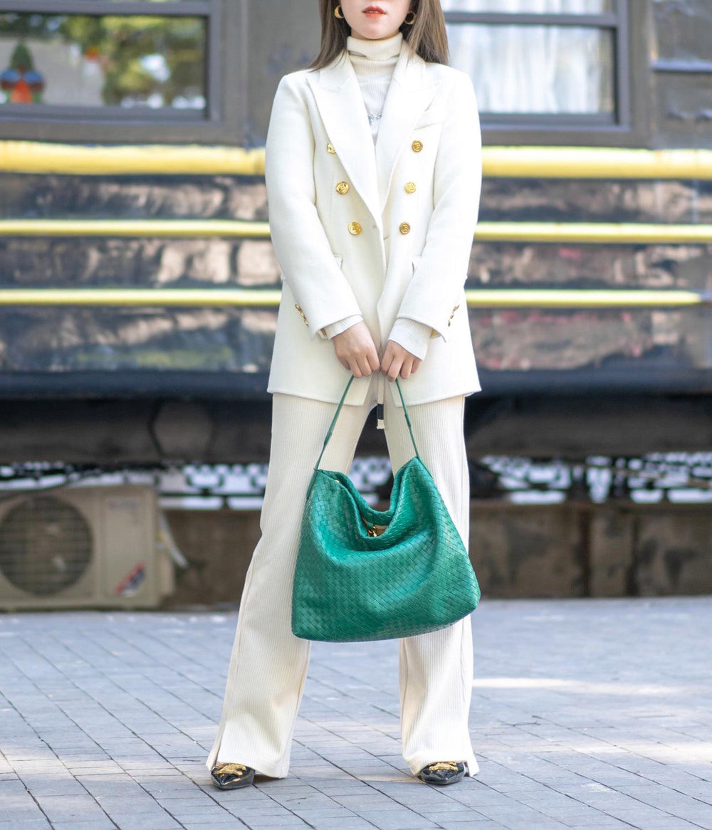 Woman in white suit holding large green woven lambskin leather tote bag