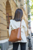 Woman wearing a white blazer with a large brown woven leather tote bag outdoors