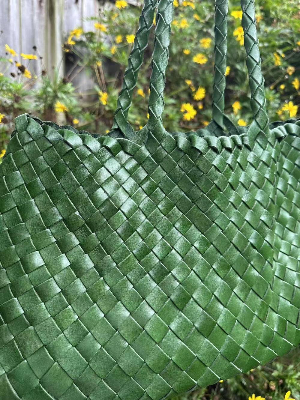 Green full grain leather woven hobo bag with braided handles, outdoor floral background