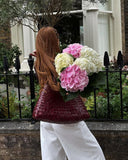 Woman carrying burgundy woven leather hobo bag and bouquet of hydrangeas outdoors