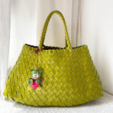 Green woven leather hobo bag with top handles and a bear keychain against a white background