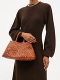 Woman holding trapezoidal woven leather hobo bag with bamboo-style handles