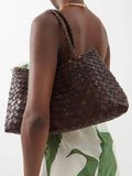 Woman carrying a dark brown woven leather hobo bag with trapezoidal shape