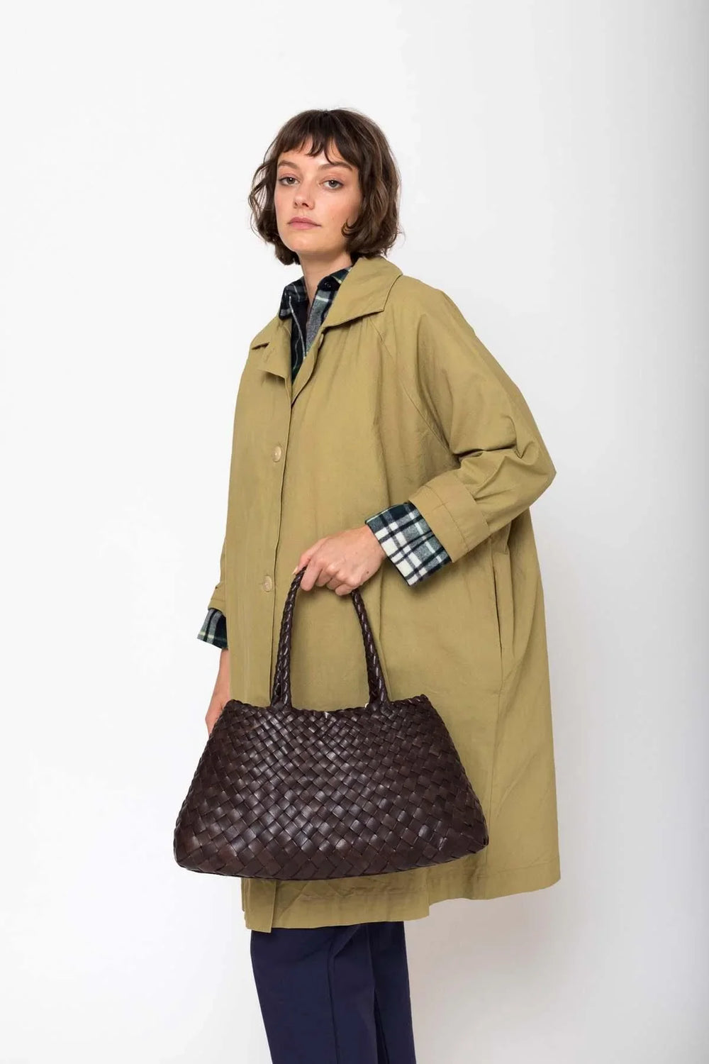 Woman holding a dark brown woven leather handbag with double handles, styled for casual wear.