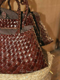 Handcrafted brown woven leather hobo bag with braided handles, displayed in a basket