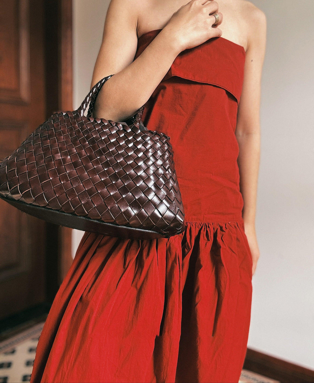 Woman in red dress holding a brown woven leather hobo trapezoidal handbag