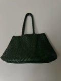 Dark green woven leather trapezoidal hobo bag with double handles on a light background