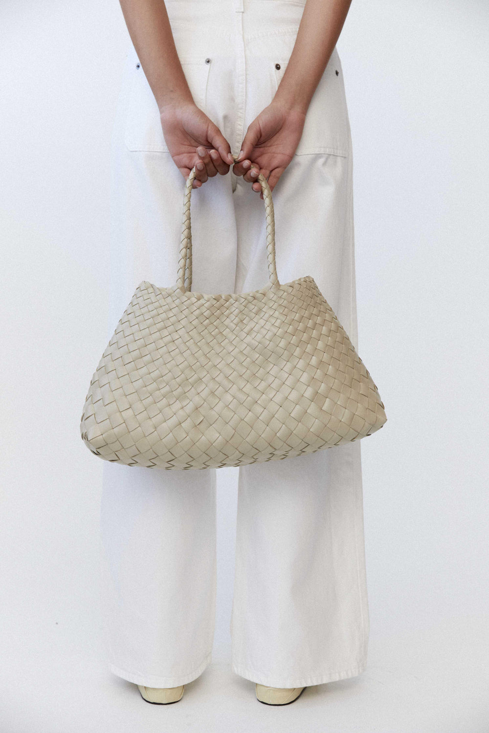 Woman holding trapezoidal woven leather hobo bag with braided handles, neutral pearl white