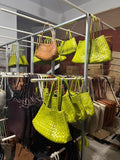 Handcrafted woven leather tote bags in lime green and brown on display racks in a showroom.