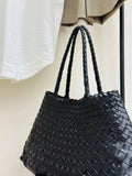 Woman holding black woven leather hobo bag with dual handles, stylish and trapezoidal shape black