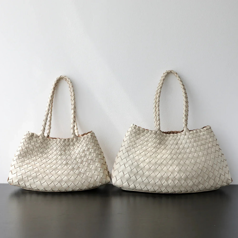 Two cream woven leather hobo shoulder bags with long braided handles on a black surface