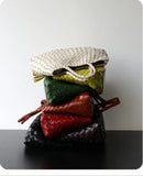 Stack of woven leather hobo shoulder bags in assorted colors on a black surface
